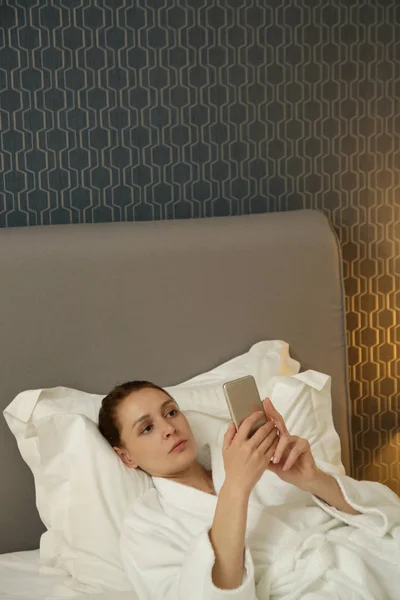 Young Woman Lying Bed Checking Messages Her Phone — 스톡 사진