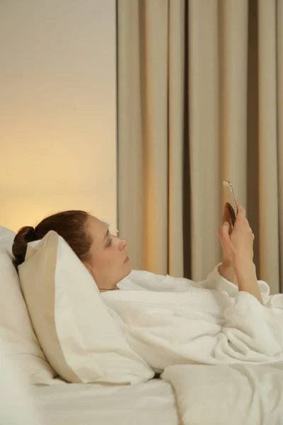 Молодая Женщина Лежит Постели Проверяет Сообщения Телефоне — стоковое фото
