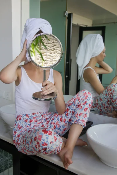 一个美丽的年轻女子 头上的毛巾站在浴室 检查她的脸在镜子 皮肤护理和反年龄的概念的肖像 — 图库照片