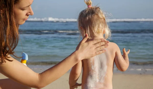 Suncare on the beach. Mother applying sunscreen protection cream to her toddler