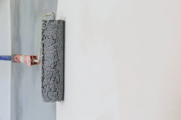 Paint roller. Painting with gray paint over a white wall