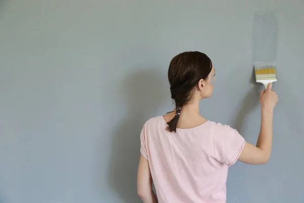 Woman painting with gray paint over a white wall