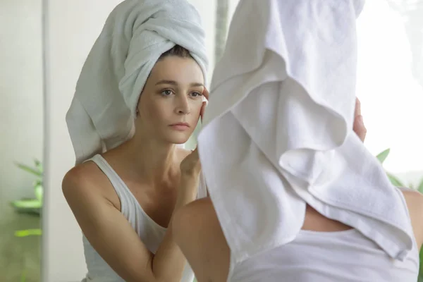一个美丽的年轻女子 头上的毛巾站在浴室 检查她的脸在镜子 皮肤护理和反年龄的概念的肖像 — 图库照片