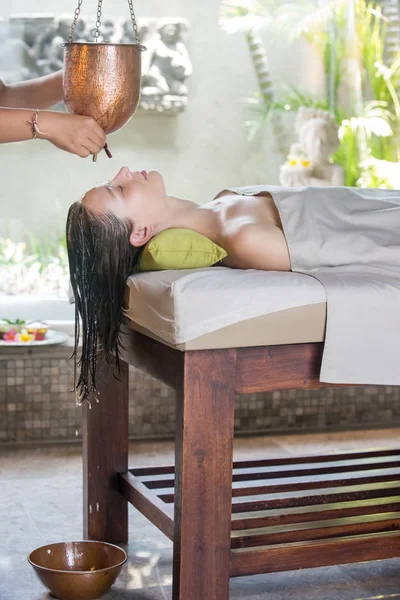 Shirodhara, an Ayurvedic healing technique. Oil dripping on the female forehead. Portrait of a young woman at an ayurvedic massage session with aromatic oil dripping on her forehead and hair.