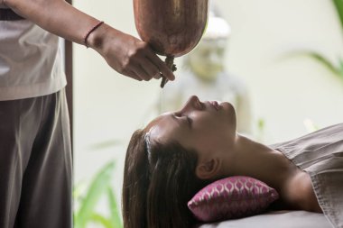 Shirodhara, Ayurveda şifa tekniği. Kadın alnına yağ damlıyor. Alnına ve saçına damlayan aromatik yağ ile ayurvedik masaj oturumunda genç bir kadının portresi.