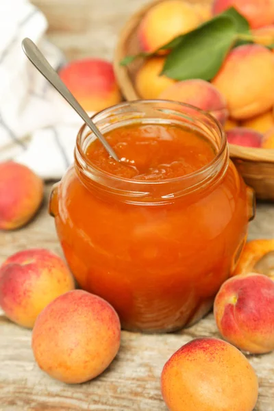 Jar of apricots jam and fresh apricots on wooden background