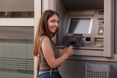 Bir bankanın önünde genç bir kadın, sokakta ATM makinesi, kart tutan 