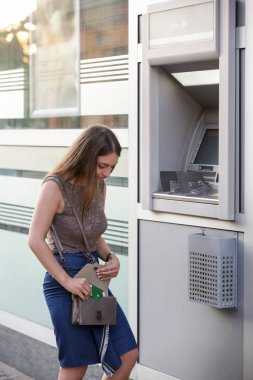 Bir bankanın önünde genç bir kadın, sokakta ATM makinesi, kart tutan 