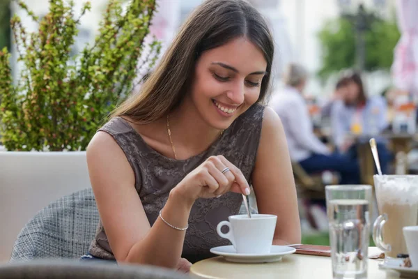Bir kafede oturan ve bir kahve şeker ekleyerek genç bir güzel kadın Portresi