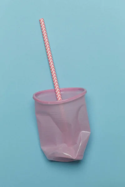 Single-use plastic problem - used plastic glass and drinking straw on the colorful background