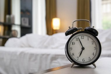 Arka planda bir yatak odası ile saat yedi gösteren komiyerde Klasik siyah çalar saat