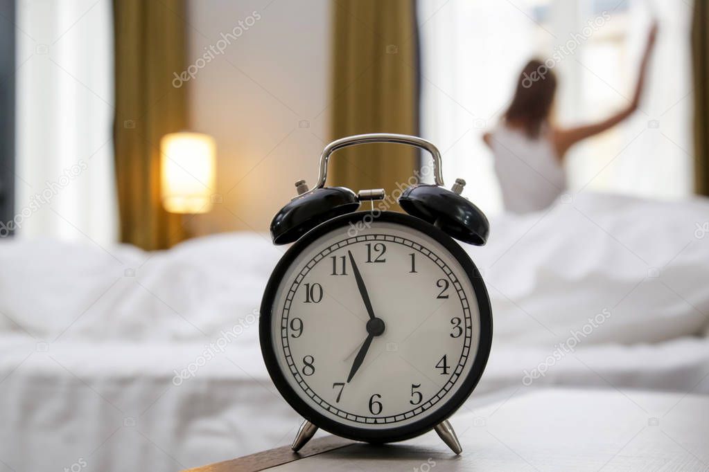 Young beautiful woman waking up and stretching at seven o clock in the morning, a good start of the day