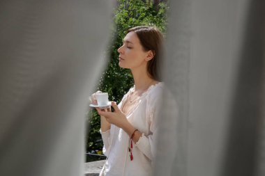 Sabah kahvesini içen beyaz ve şık bir kadının şehrin balkonunda portresi