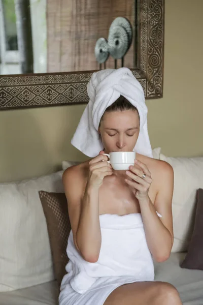 若い白人女性は 朝のコーヒーを持ってタオルに包まれ その日の準備をしています — ストック写真