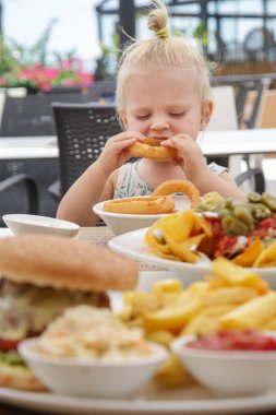 Sevimli sarışın bebek kız restoran masada oturan ve soğan halkaları yeme