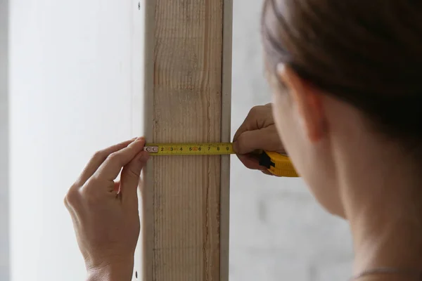 Woman holding a meter, measuring dimensions on plasterboard panel - DIY home improvement concept