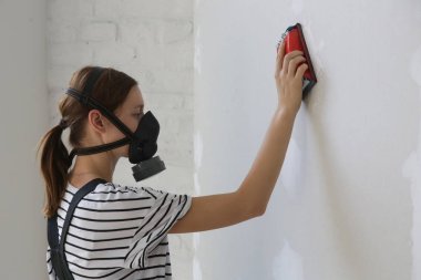 Çalışan toz koruyucu maske takan genç kadın ve zıpzAma duvarı ile zıpkınlama bloğu ile kaymak kaplama sonra. Boyama dan önce hazırlık. Yenileme evi konsepti.