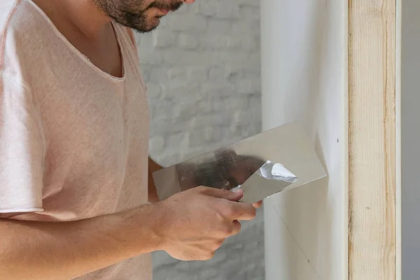 Man plastering wall with putty-knife. Fixing wall surface and preparation for painting. DIY housing improvement project.