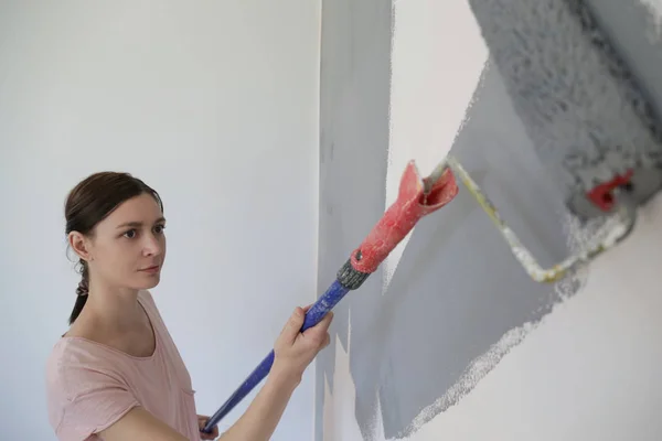 Женщина Рисует Серой Краской Над Белой Стеной — стоковое фото