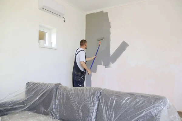 Man painting with gray paint over a white wall