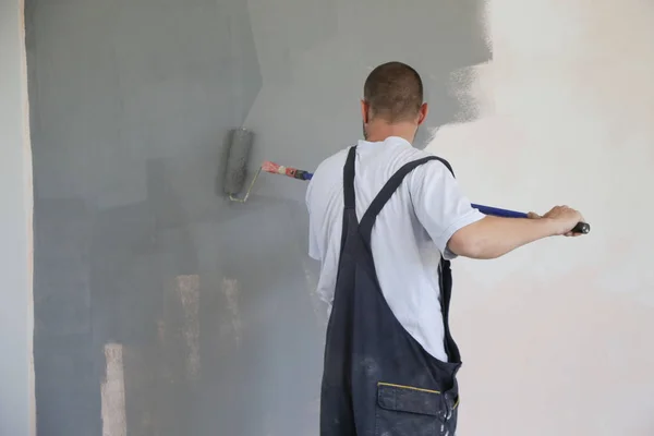 Man painting with gray paint over a white wall