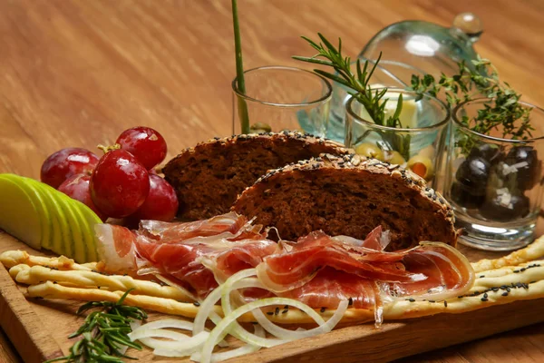 Traditional Italian appetizer board with prosciutto, bread and condiments served on the wooden restaurant table. Exquisite dish. Creative restaurant meal.