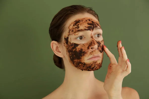 Woman exfoliating face with a coffee scrub, studio shot.