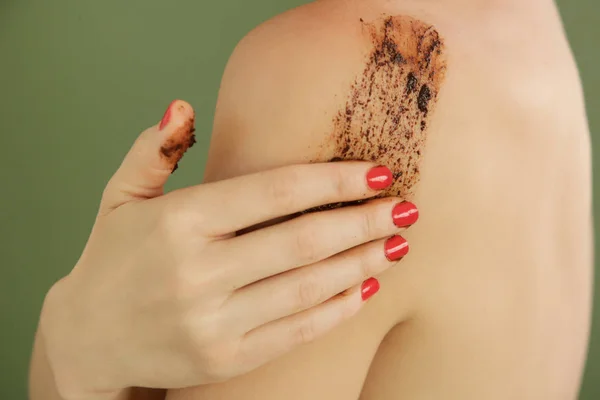 Woman applying coffee scrub on her body, close up studio shot.