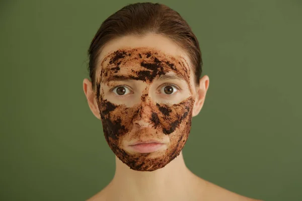 Woman exfoliating face with a coffee scrub, studio shot.