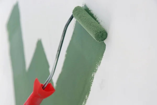 Paint roller. Process of painting with green paint over a white wall.