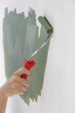 Boya rulosu. Beyaz bir duvar üzerinde yeşil boya ile boyama süreci.