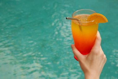 Yüzme havuzunun yanında büyük bir kokteyl bardağı tutan bir kadın resmi. Yaz tatili eğlence aktivitesi.