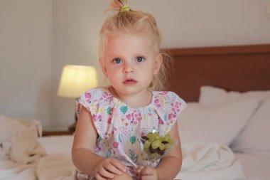 Sevimli küçük kız yatakta oturuyor ve bir kaseden üzüm yiyor.