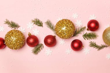 Altın ve kırmızı Noel topları ve soluk pembe arka planda köknar dalları. Noel süsü aranjmanı.