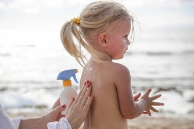 Annem küçük şirin bir kıza güneş kremi sürüyor.