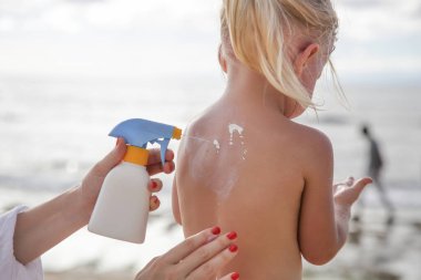 Annem küçük şirin bir kıza güneş kremi sürüyor.