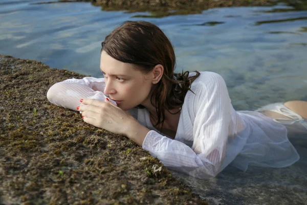 若い白人女性が海岸にポーズをとっている 干潮時に海のビーチで白いシャツを着た女の子 — ストック写真