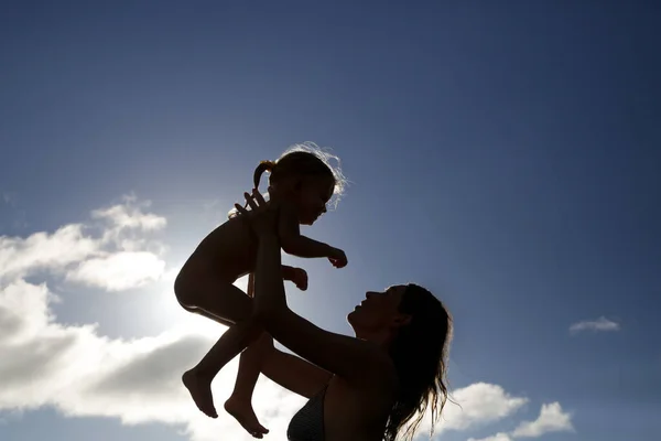 Silhouette of mother and baby at sunset. Mother throwing child up in the air.
