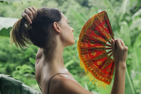 Woman fighting heat wave with a fan. Outdoor portrait of a young woman in a park during a hot summer day.