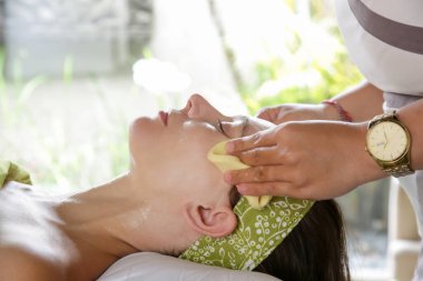 Deri ve vücut bakımı. Yüzüne spa tedavisi yaptıran genç bir kadının yakın çekimi. Yaş karşıtı yüz masajı.