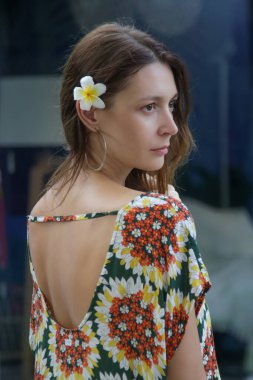Kulağının arkasında Frangipani çiçeği olan renkli elbiseli şık bir kadının açık hava portresi. Gündelik yaz hippi kıyafetleri, bahar-yaz moda trendi, tropik tatil tarzı..