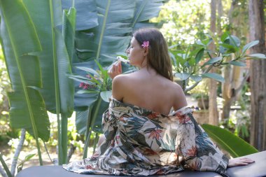 Açık hava spa salonunda masaj bekleyen ipek bornozlu rahat genç bir kadın.