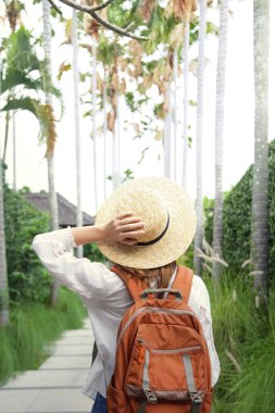 Yaz tatilinde hasır şapka ve turuncu sırt çantası takan turist kadının arkası..