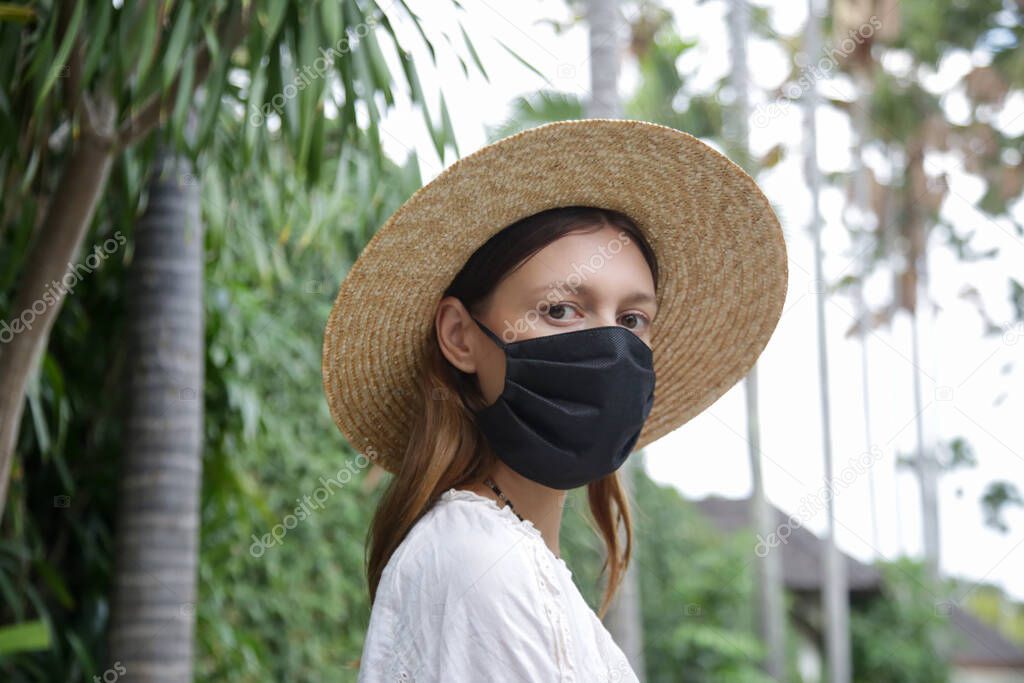 Tourist woman wearing protective face mask. Woman wearing straw hat, medical mask and backpack on her summer vacation. Tourism during coronavirus outbreak.