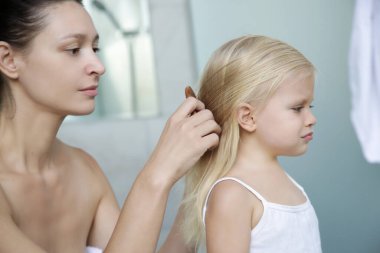 Anne küçük kızının saçını banyoda tarıyor. 