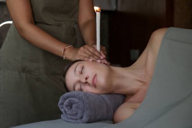 Spa 'da kulak mumu tedavisi gören bir kadın. Kulak konisi ya da termal auriküler terapi.