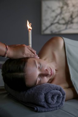 Spa 'da kulak mumu tedavisi gören bir kadın. Kulak konisi ya da termal auriküler terapi.