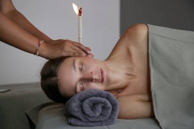 Spa 'da kulak mumu tedavisi gören bir kadın. Kulak konisi ya da termal auriküler terapi.