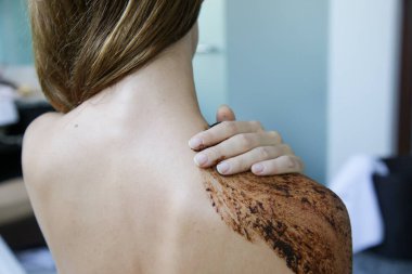 Kahve fırçası. Güzel cilt bakımı. Genç bir kadın omuzlarına ve boynuna kahve fırçası sürüyor..