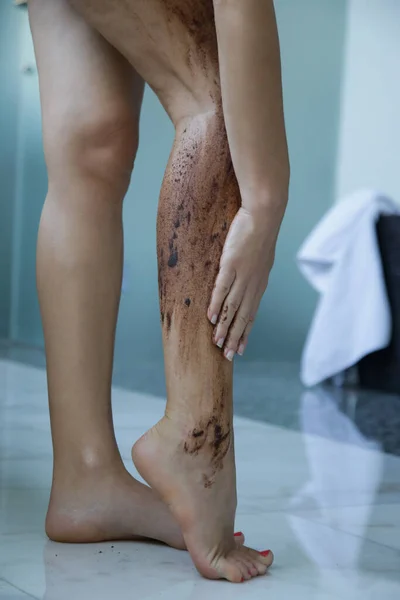 DIY Coffee scrub. Beauty skin care. Young woman putting coffee scrub on her legs.